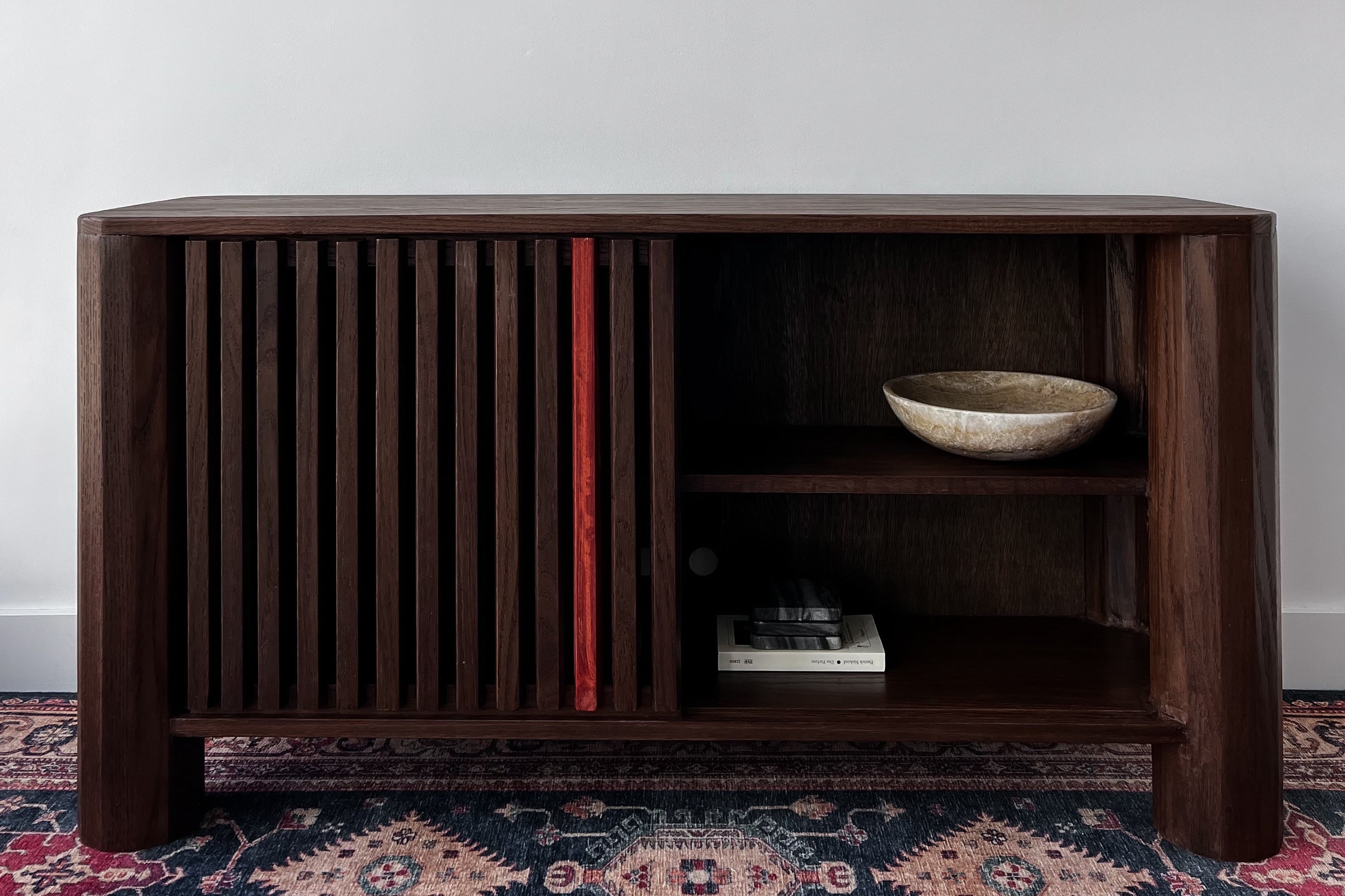 Wooden sideboard with a bowl on a patterned rug against a white wall. Red Line Furniture