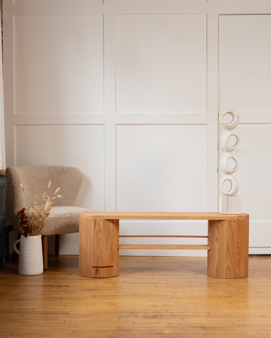 Handmade red oak iB-v2 Dual Column Bench by Redline Design with its signature red line, beside a boucle chair