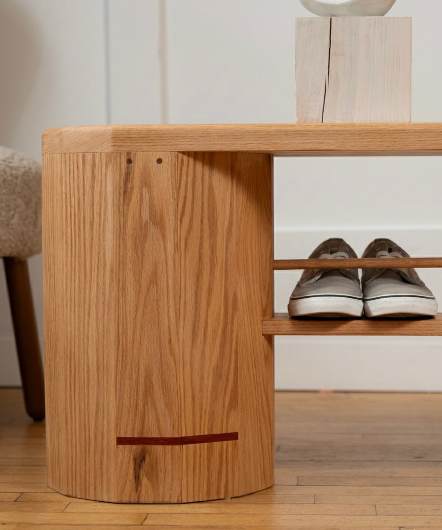 Close-up of the iB-v2 Dual Column Bench in red oak showing the wood grain, signature red line and a lower shoe shelf