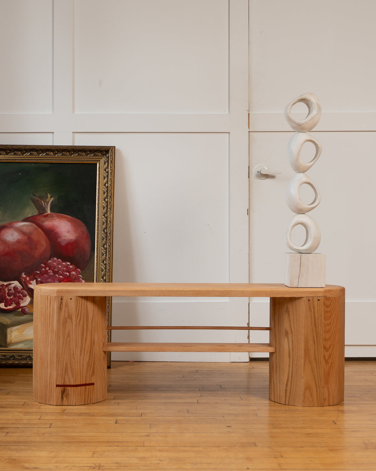 iB-v2 Dual Column Bench in red oak with its signature red line, styled with a pomegranate painting and stacked sculpture